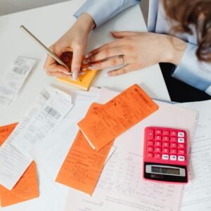 A woman writes down financial details using a calculator, receipts, and documents.